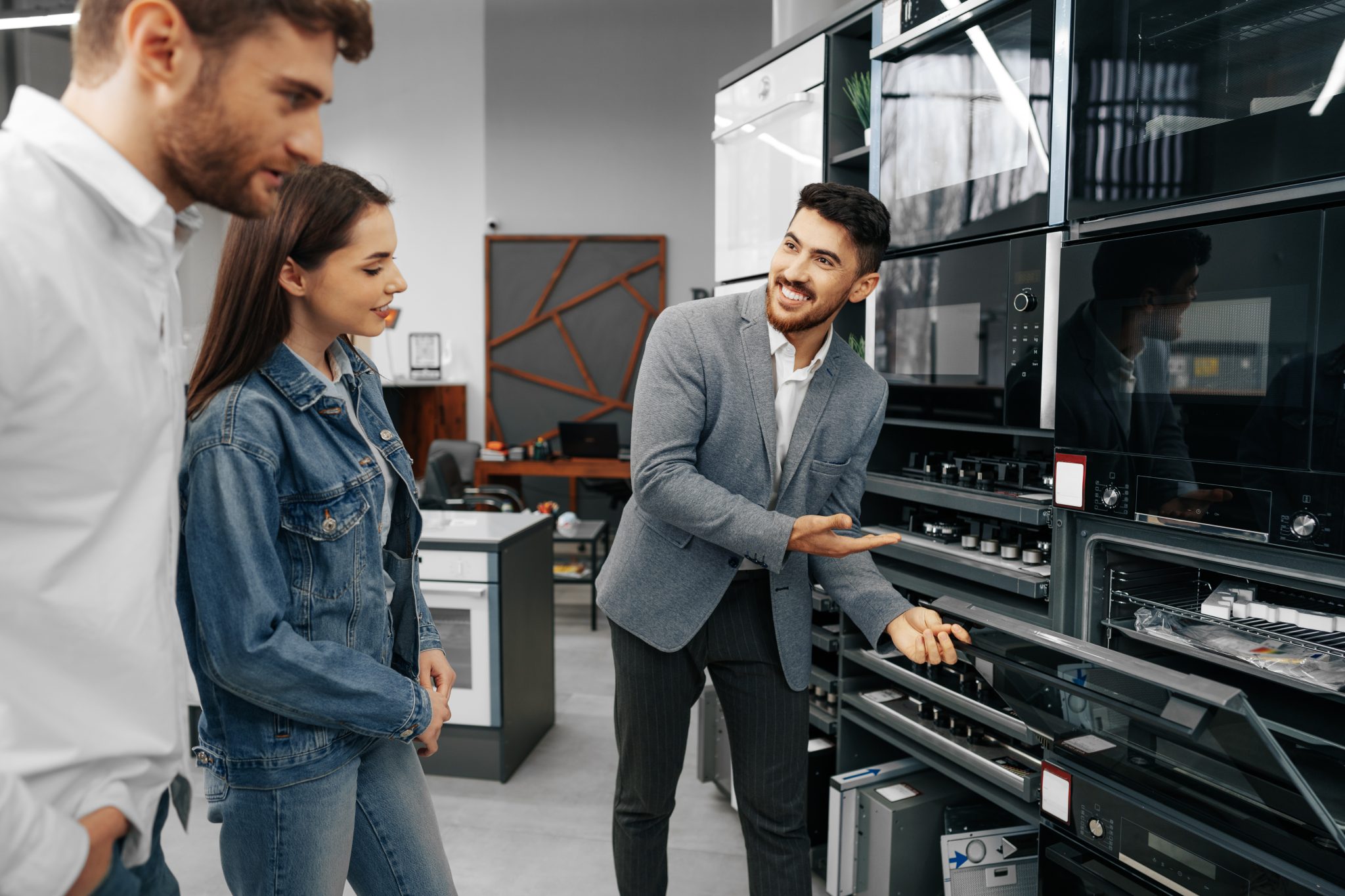 Male shop assistant helps young couple to choose new home appliance in hypermarket